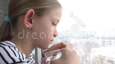 生病的孩子望着窗外，悲伤的孩子脸在喝茶，暴风雪的冬天